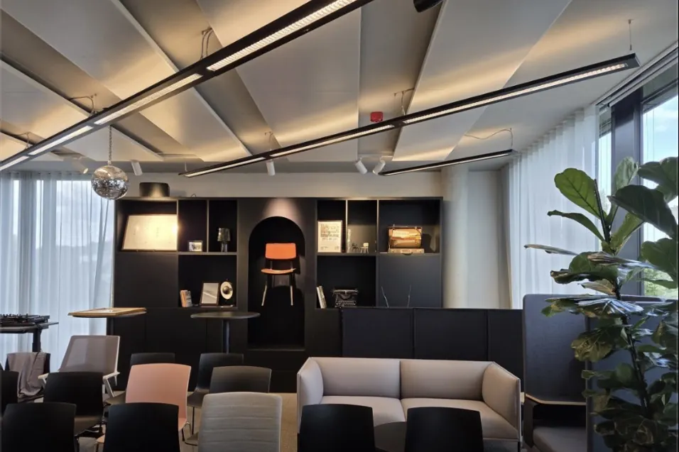 Büro-Lounge mit langen LED-Linienleuchten unter Akustikdecke, Strahlern und Regalwand – Bürobeleuchtung von ElektroTechnik Posengis