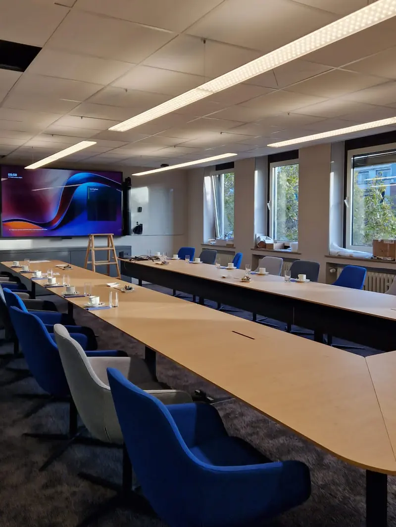 Besprechungsraum nach dem Büroumbau mit LED-Pendelleuchten, großem Display an der Medienwand und Tischanschlüssen im Konferenztisch