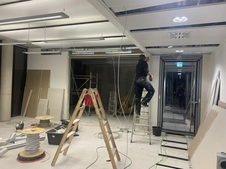 Elektriker von ElektroTechnik Posengis auf der Leiter bei der Installation während eines Büroumbaus – offene Decke, Kabeltrommeln und neue Leitungswege