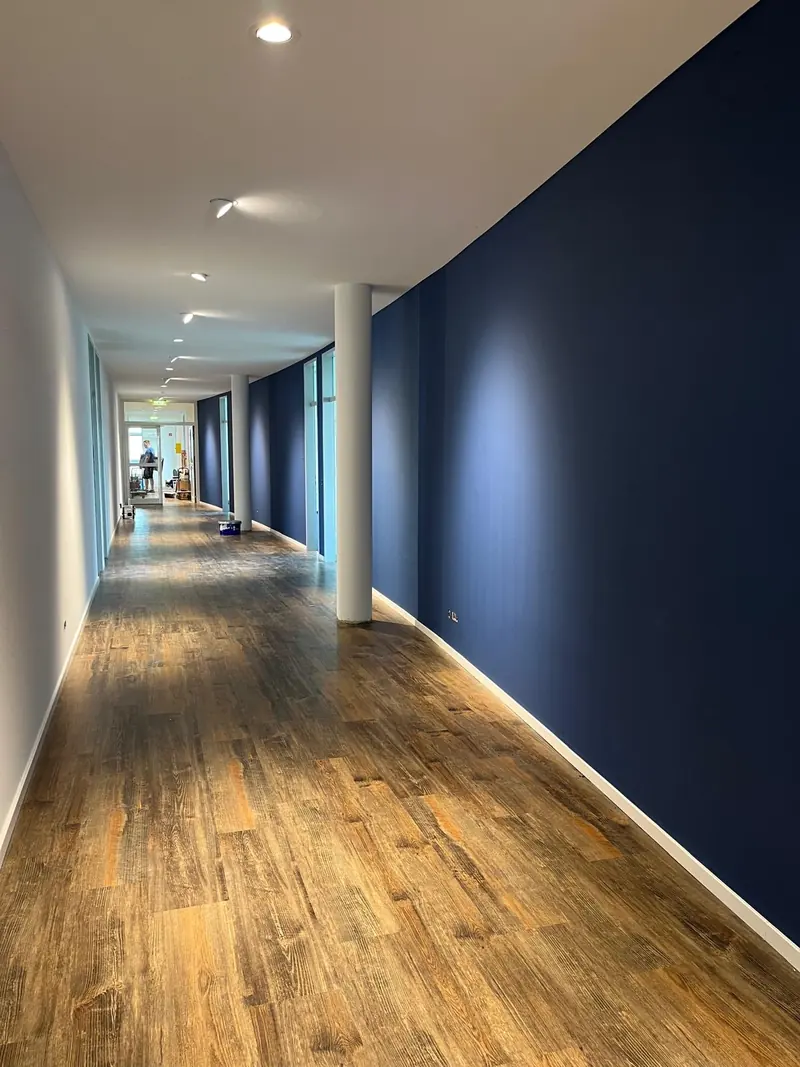 Büroflur mit dunkelblauer Wand, die von schwenkbaren LED-Einbaustrahlern angestrahlt wird