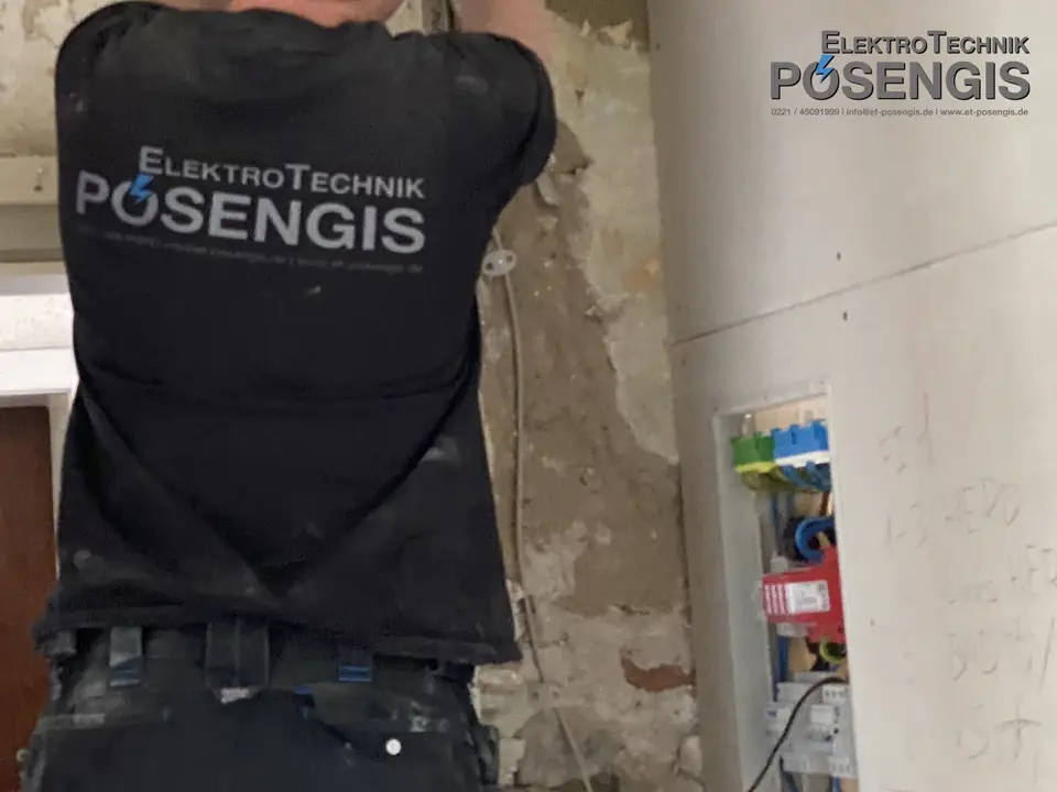 Monteur von ElektroTechnik Posengis bei der Elektrosanierung eines Altbaus: aufgestemmte Wand mit neuer Leitungsführung und geöffneter Unterverteilung mit Überspannungsschutz