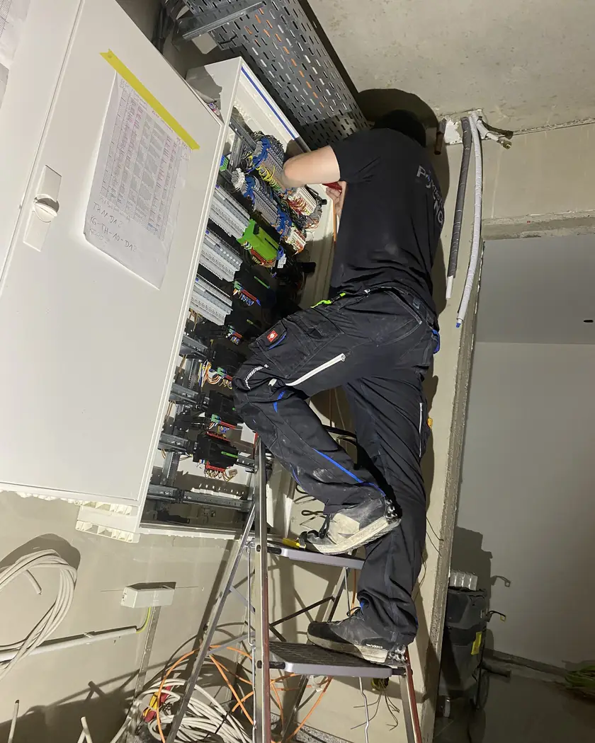 Monteur von ElektroTechnik Posengis auf einer Leiter bei der Verdrahtung eines großen Verteilerschranks in einem Gewerbeobjekt