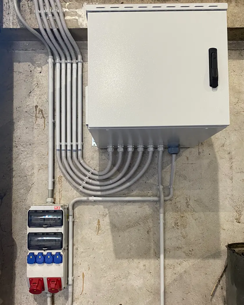 Saubere Aufputz-Installation im Keller: Verteilerschrank mit parallel geführten Installationsrohren und darunter eine Steckdosenkombination mit Schutzkontakt- und CEE-Drehstromsteckdosen