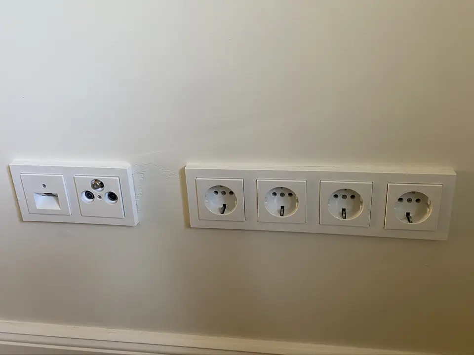 Fertige Feininstallation an einer Wohnzimmerwand: Netzwerkdose und TV-Anschlussdose in einem Zweifachrahmen, daneben eine Vierfach-Steckdose
