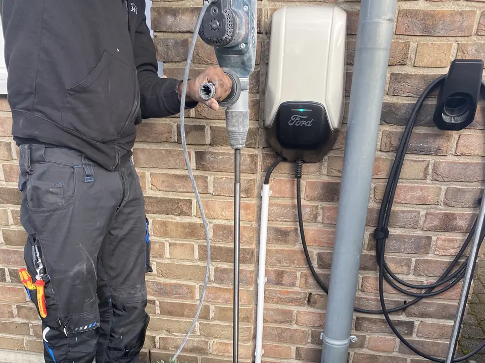 Monteur schlägt mit einem Bohrhammer einen Staberder neben einer Wallbox an der Hauswand ein
