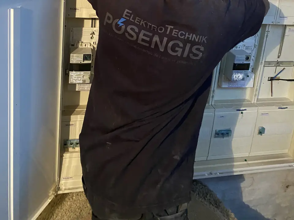 Monteur von ElektroTechnik Posengis an geöffneten Zählerschränken in einem Mehrfamilienhaus mit elektronischen Zählern