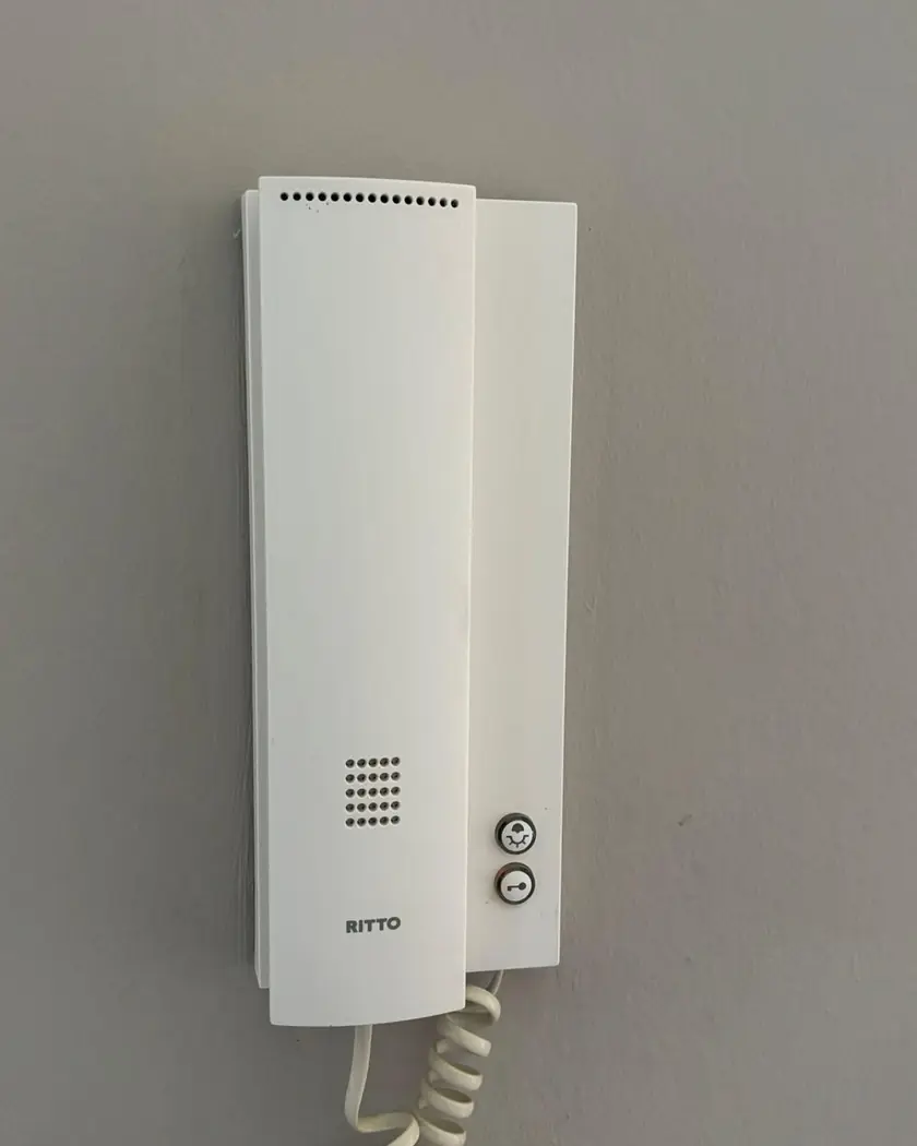 Älteres weißes Audio-Haustelefon mit Hörer und Spiralkabel an einer grauen Wand
