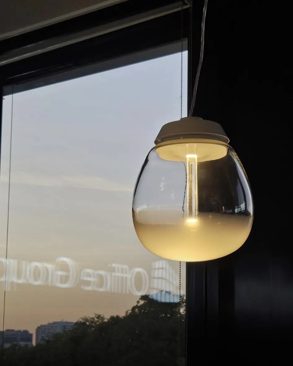 Gläserne LED-Pendelleuchte mit warmem Licht vor einem Fenster in der Abenddämmerung