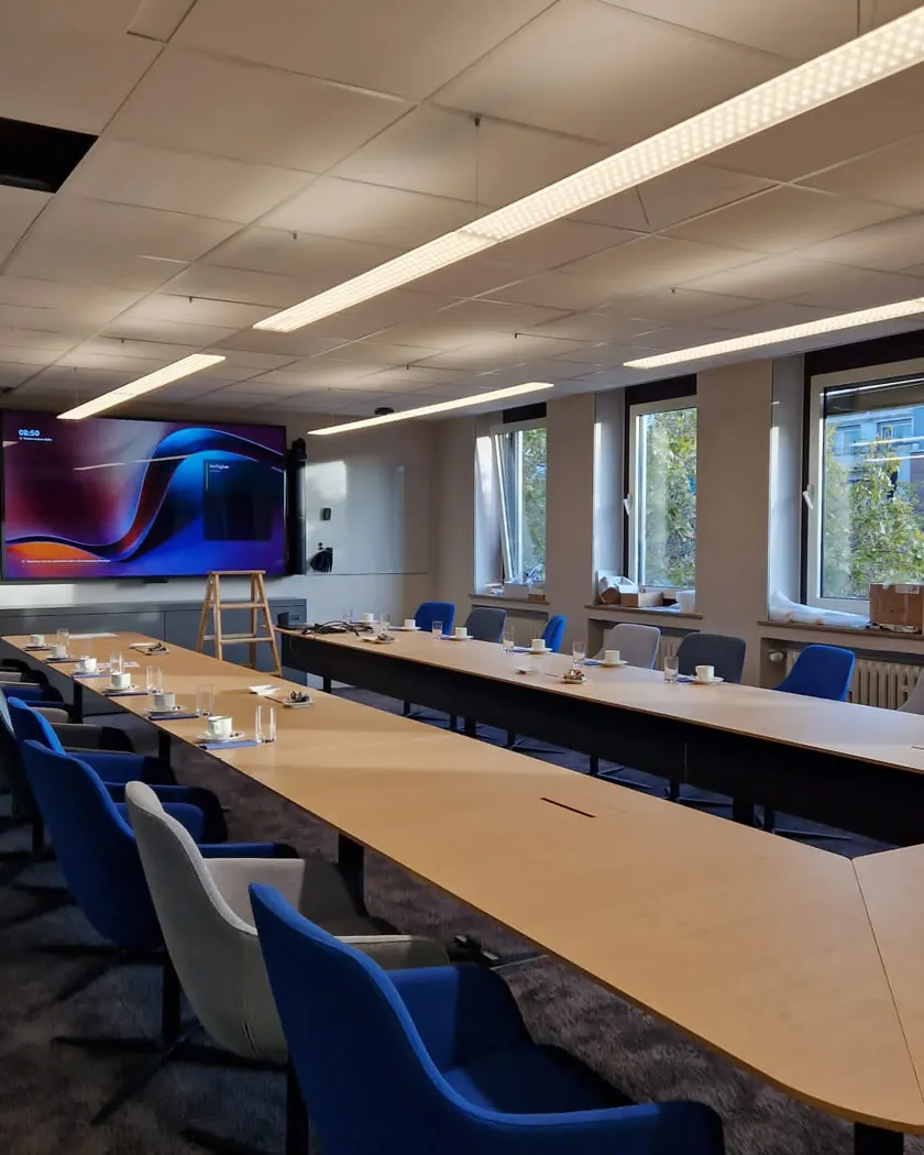 Besprechungsraum nach dem Büroumbau mit langen LED-Pendelleuchten über dem Konferenztisch, Medienwand mit Display und Tischanschlüssen