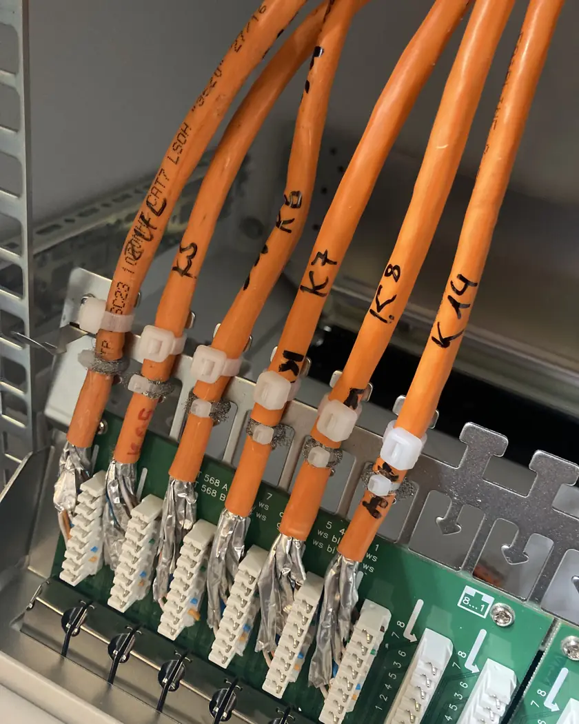 Orangefarbene geschirmte Cat.7-Datenkabel, beschriftet mit K5 bis K14, aufgelegt auf die LSA-Anschlussleisten eines Patchfelds
