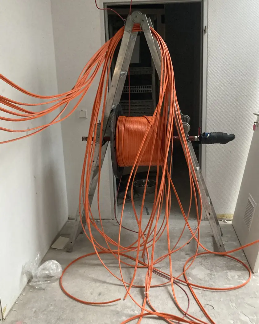 Kabeltrommel mit orangefarbenem Netzwerkkabel auf einem Leiterbock, davon ausgehend zahlreiche Leitungen, die in einem Flur zur Decke eingezogen werden
