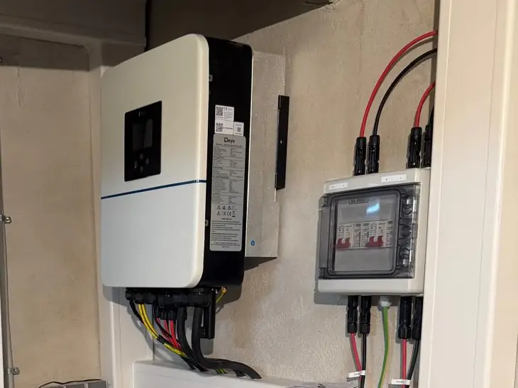 Hybrid-Wechselrichter mit Anschlussleitungen, daneben ein DC-Generatoranschlusskasten mit Überspannungsschutz und roten und schwarzen Solarleitungen