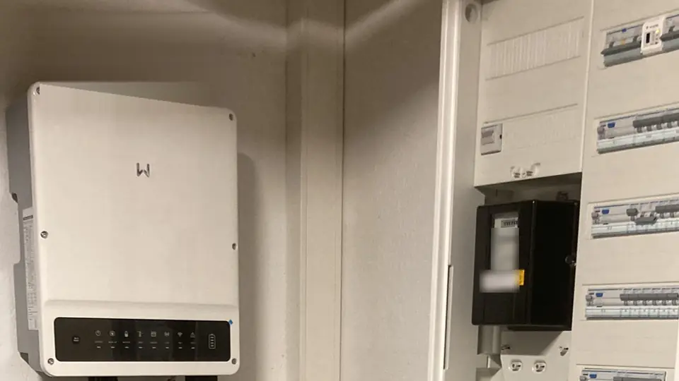 Hybrid-Wechselrichter an der Kellerwand neben einem geöffneten Zählerschrank mit Zähler, Leitungsschutzschaltern und FI-Schutzschaltern