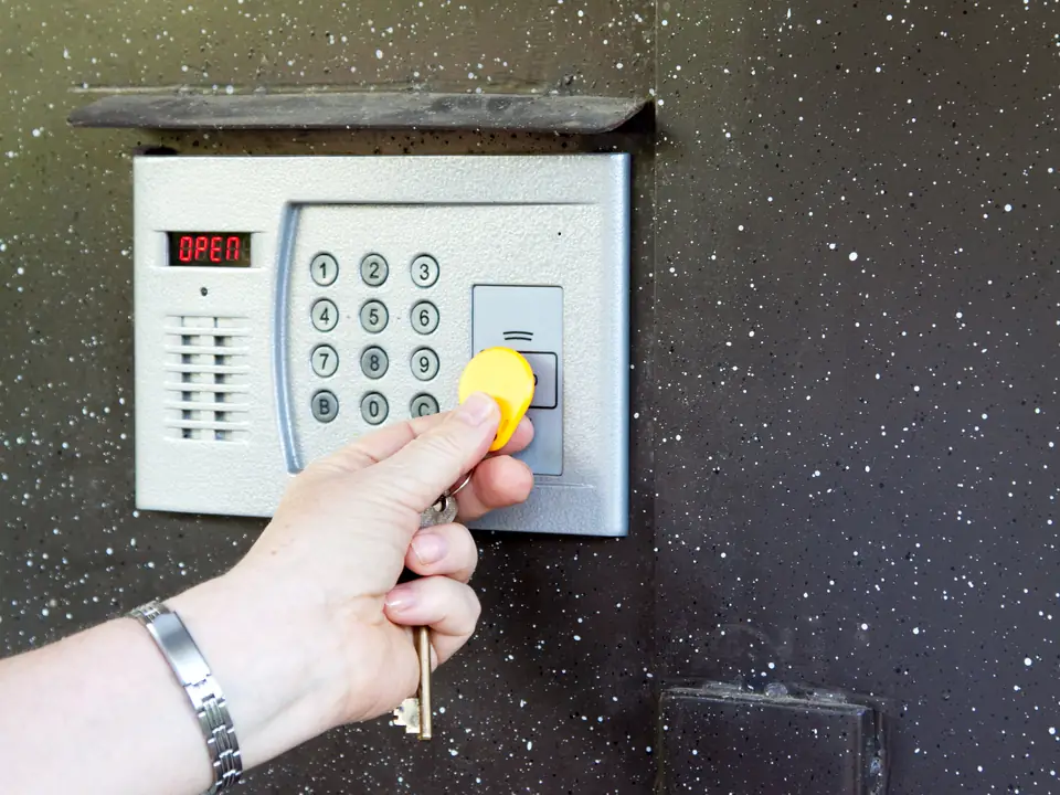 Hand hält einen gelben Transponder-Chip an ein Bedienteil mit Zifferntastatur und Anzeige an einer Wand