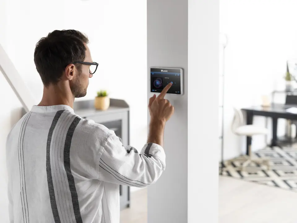 Mann bedient ein an der Wand montiertes Touchpanel eines Smart-Home-Systems in einer hellen Wohnung